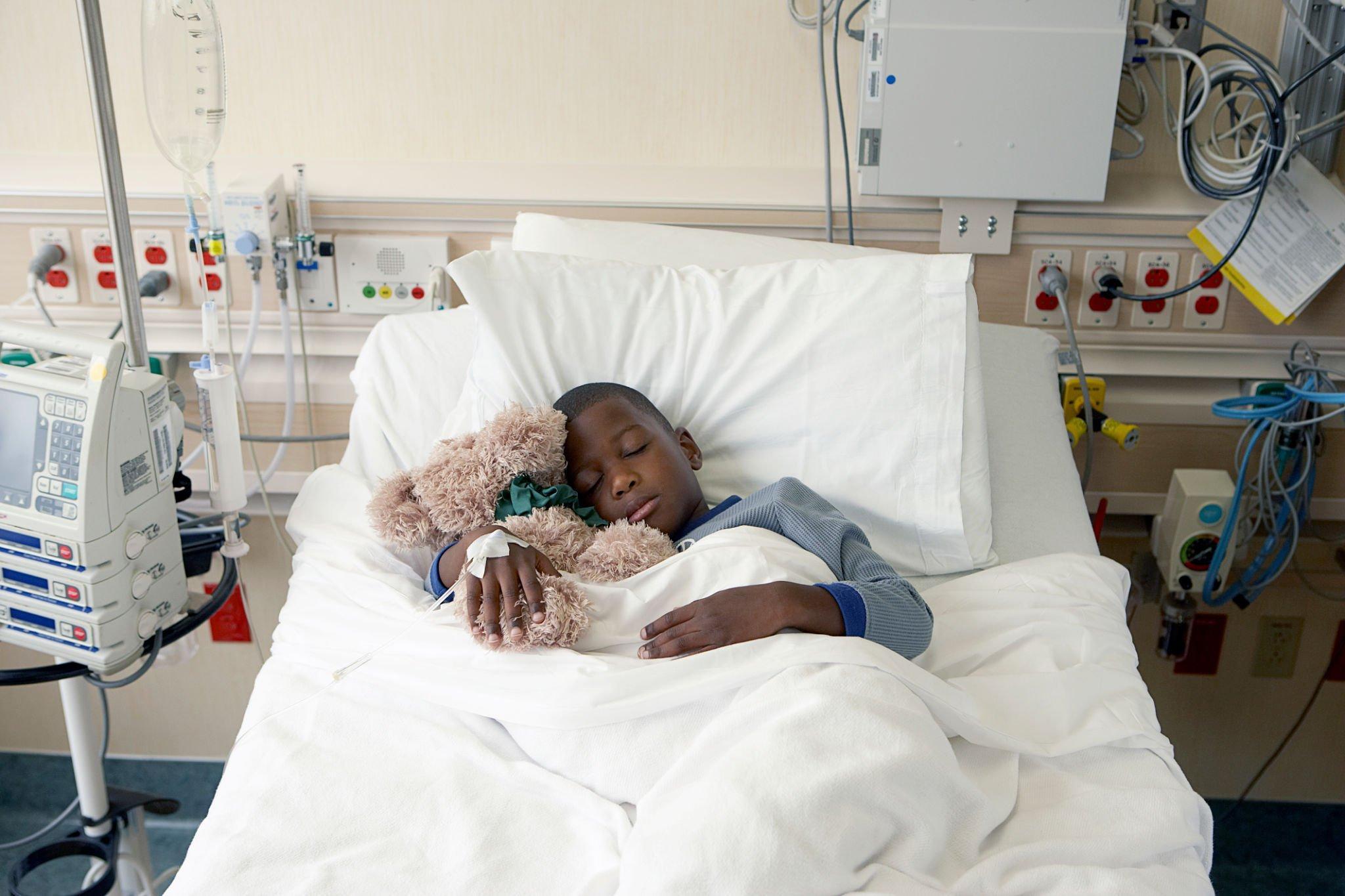 a little boy holding a teddy while sleeping on a hospital bed
